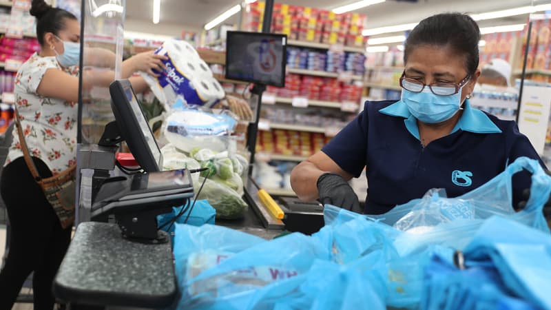Olga Jiminez se tient derrière un écran de protection partielle en plastique et porte un masque et des gants alors qu'elle travaille comme caissière au supermarché Presidente le 13 avril 2020 à Miami, en Floride. (Photo d'illustration)
