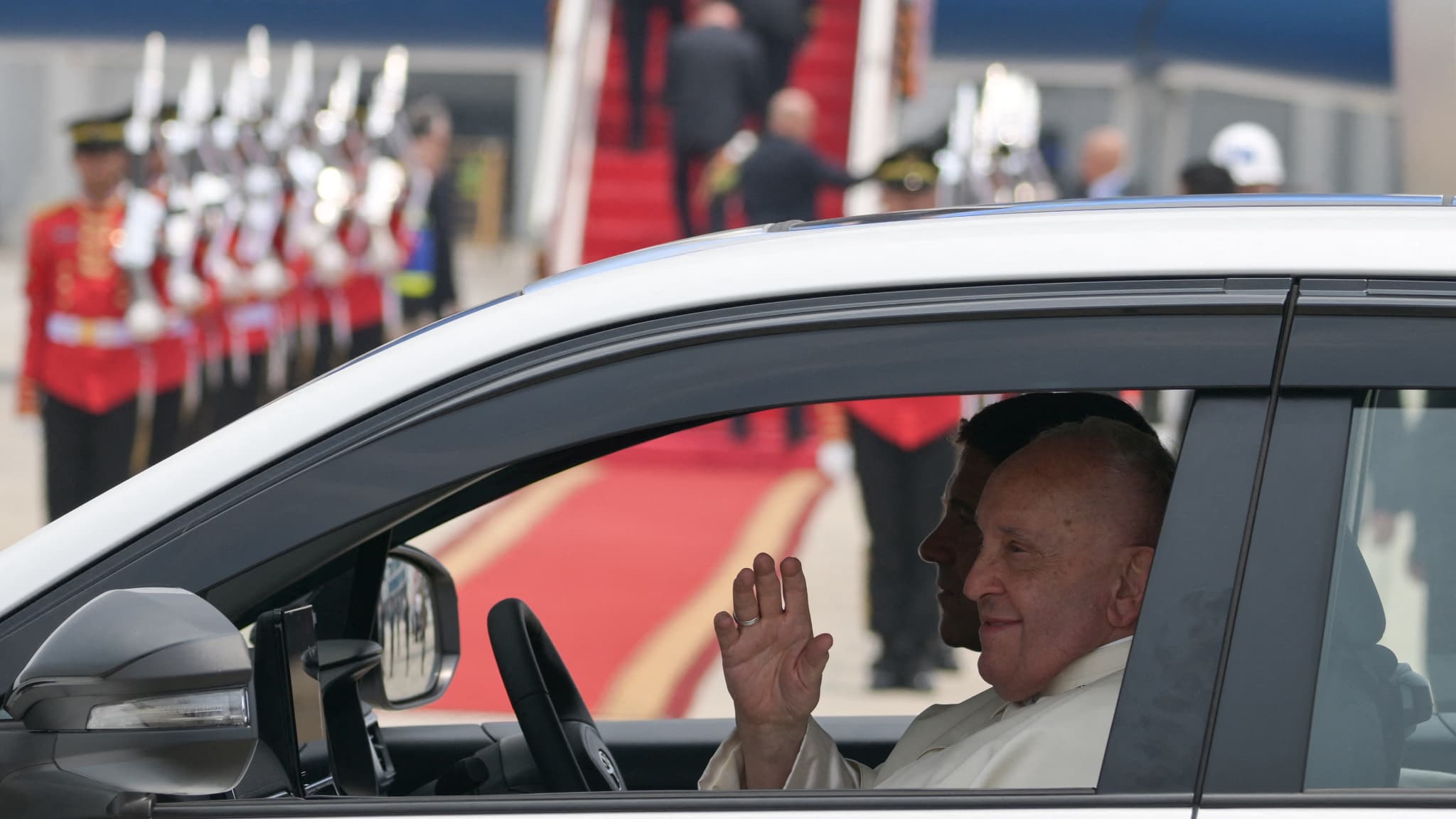 Le pape François salue depuis un véhicule en partance après son arrivée à l'aéroport international Soekarno-Hatta de Jakarta, le 3 septembre 2024. 