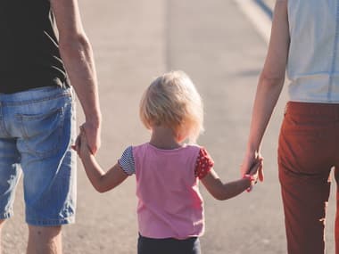 Une enfant tenant la main à ses parents.