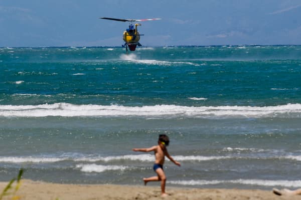 Un garçon joue sur le front de mer alors qu'un hélicoptère de lutte contre les incendies plane au-dessus de la mer pour remplir de l'eau afin de lutter contre les feux de forêt près du village de Loutses sur l'île grecque de Corfou, le 27 juillet 2023.
