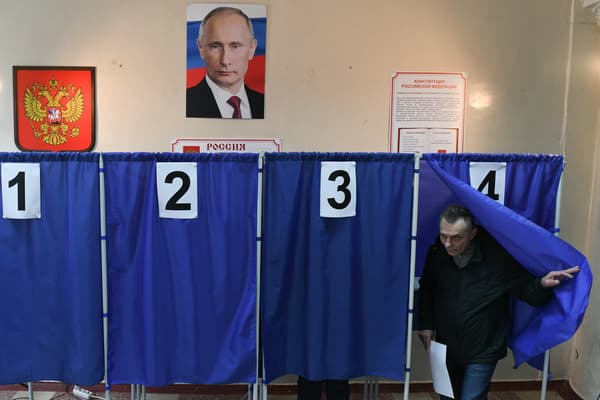Un homme vote lors de l'élection présidentielle russe, sous un portrait de Vladimir Poutine, dans un bureau de vote à Donetsk, en Ukraine contrôlée par la Russie, le 16 mars 2024.