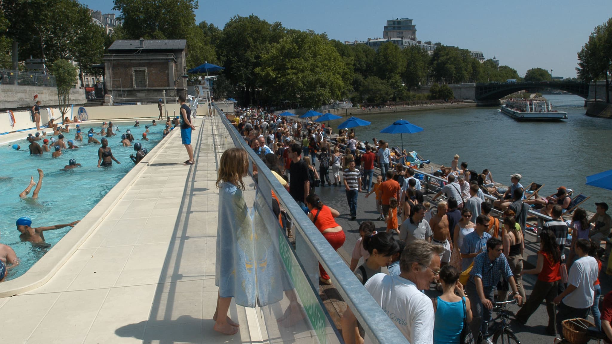 Des visiteurs se promènent sur les quais de la Seine tandis que des enfants profitent du bassin de baignade aménagé dans le cadre de la 3e édition de l'opération Paris-plage, le 24 juillet 2004
