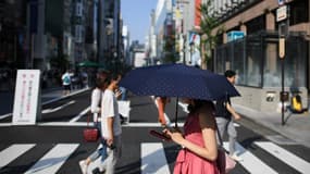 Une femme en train de traverser la rue près de Tokyo, les yeux rivés sur son smartphone.