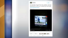 Un journaliste de The Weather Channel semble lutter contre le vent, alors que deux hommes marchent tranquillement derrière lui. 