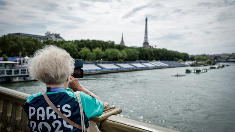 Une bénévole des JO-2024 prend une photo sur le pont des Invalides à côté des tribunes installées sur la Seine à la veille de la cérémonie d'ouverture des Jeux Olympiques 2024, à Paris, le 25 juillet 2024