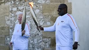 L'ancien footballeur français Basile Boli (d) allume le flambeau de Colette Cataldo, supportrice historique de l’OM dans le cadre des relais de la flamme olympique et paralympique à la basilique Notre Dame de la Garde, à Marseille, le 9 mai 202