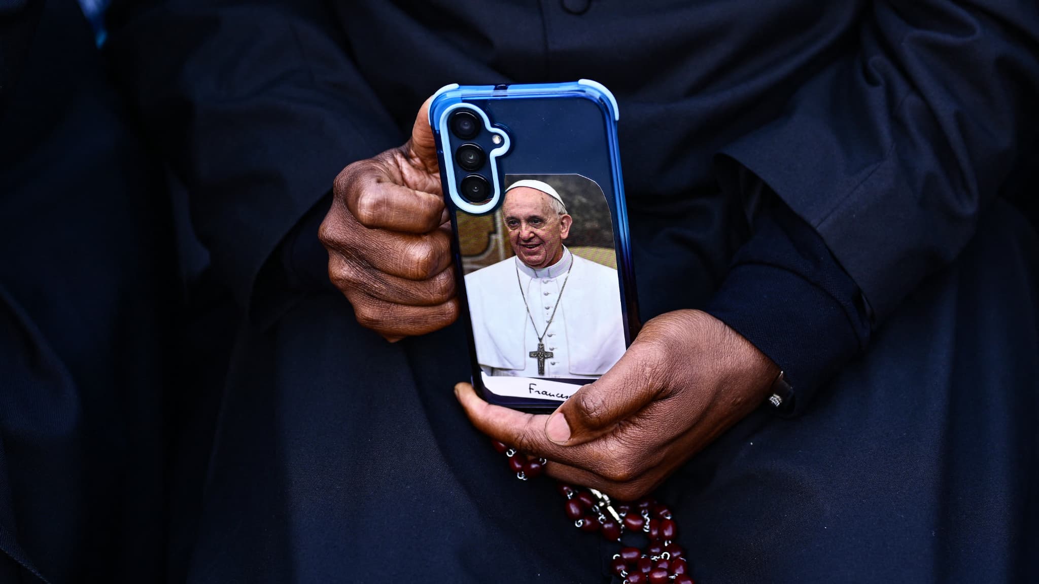 Un homme tient son smartphone avec une photo du pape François dans l'étui du téléphone et un chapelet pendant une prière sur la place Saint-Pierre, un jour après la mort du pape, au Vatican, le 22 avril 2025. Un homme tient son smartphone avec une photo du pape François dans l'étui du téléphone et un chapelet pendant une prière sur la place Saint-Pierre, un jour après la mort du pape, au Vatican, le 22 avril 2025.