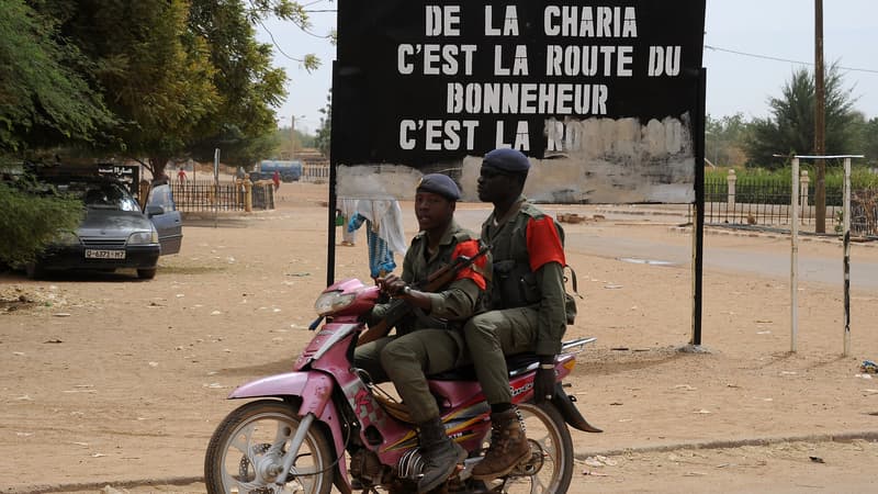 Soldats maliens circulant devant un panneau exaltant la Charia, en 2013. 