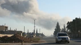 Une voiture traverse la localité de Khan al-Assal dans la province d'Alep, au nord de la Syrie, avec de la fumée en arrière-plan, alors que les djihadistes et leurs alliés se battent contre l'armée syrienne dans la région, le 29 novembre 2024.