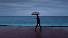 ILLUSTRATION - Un passant s'abrite de la pluie sous un parapluie, le long de la plage sur la "Promenade des Anglais" à Nice, le 30 octobre 2023
