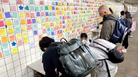 Des passagers du métro de New York apposent des Post-it sur le mur d'une station, novembre 2024