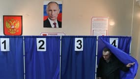 Un homme vote lors de l'élection présidentielle russe, sous un portrait de Vladimir Poutine, dans un bureau de vote à Donetsk, en Ukraine contrôlée par la Russie, le 16 mars 2024.