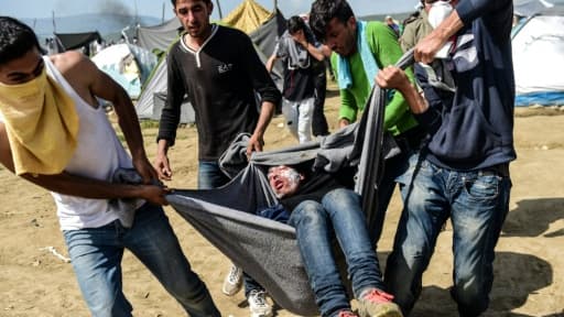 Des migrants transportent un homme blessé lors de heurts avec la police, en tentant en vain de franchir la frontière gréco-macédonienne à Idomeni, le 10 avril 2016