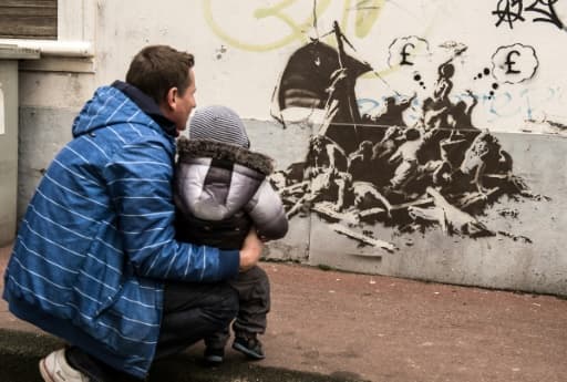 Un homme et un enfant regardent un pastiche de la célèbre toile "Le radeau de la méduse" peint par Bansky sur un mur non loin de la mairie de Calais, le 12 décembre 2015