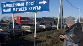 Une femme regarde son téléphone mobile près d'une file d'attente de voitures à la frontière entre l'Ukraine et la Russie, au point de passage d'Avilo-Uspenka, le 19 février 2022