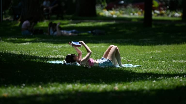 Une femme lit, allongée dans l'herbe d'un parc à Toulouse, lors d'une chaude journée, le 18 mai 2022 à Toulouse