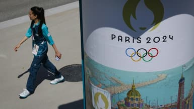 Une volontaire passant à côté d'une affiche des Jeux olympiques 2024 dans le village des athlètes le 18 juillet 2024 à Saint-Denis