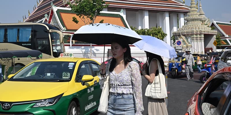 Des touristes se protègent du soleil avec des parapluies pour lutter contre la chaleur à l'extérieur du temple bouddhiste Wat Pho à Bangkok, le 1er avril 2024. 