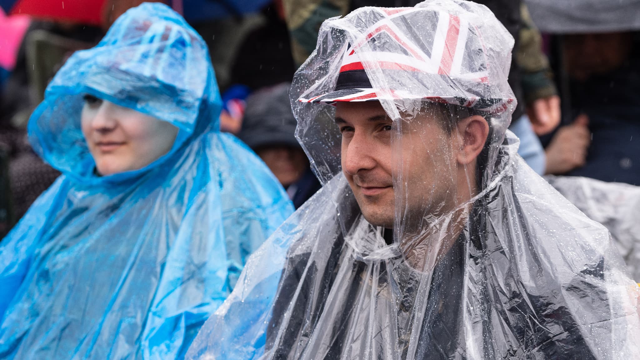 Des spectateurs attendent la procession du roi sous une pluie diluvienne, le 6 mai 2023, à Londres.