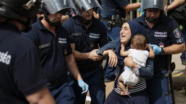 Une migrante cerclée de policiers tente de se débattre, son enfant dans les bras, le 3 septembre, à Bicske, en Hongrie.