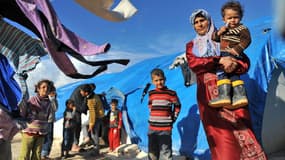 Une femme syrienne porte ses enfants dans un camp de réfugiés à la frontière turque.