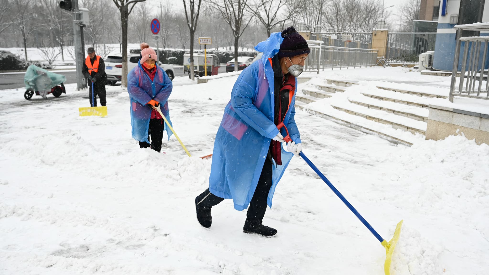 Des personnes déneigent un trottoir lors d'une journée enneigée à Pékin, le 13 décembre 2023.