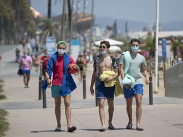 Des promeneurs avec les masques le long de la plage à Barcelone, le 18 juillet 2020
