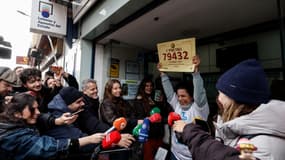 Des vendeurs de billets de loterie posent devant leur boutique, tenant en main un billet gagnant du premier prix de la loterie de Noël espagnole "El Gordo", à Madrid, le 22 décembre 2025.