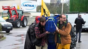 Des agriculteurs portent une statue en fer en forme de vache lors d'une manifestation devant le siège de Lactalis à Laval, le 21 février 2024 en Mayenne