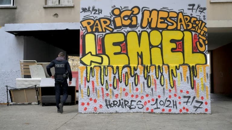 Un policier à côté d'un graffiti indiquant "Par ici mes abeilles, vous trouverez du miel ouvert 10/2h 7j/7" ,dans un point de dealer connu dans les quartiers nord de Marseille, le 1er décembre 2023