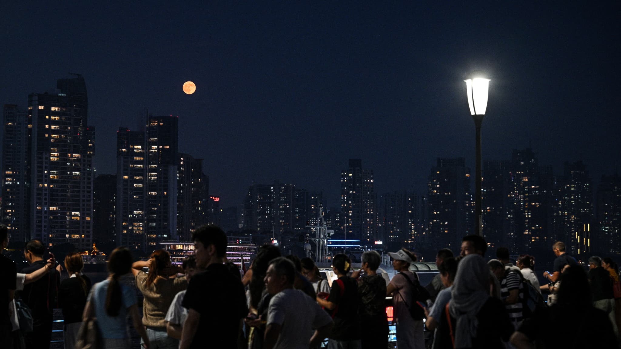 Des personnes se promènent sur la promenade du Bund, alors qu'une lune de sang, se lève dans le ciel nocturne de Shanghai, le 7 septembre 2025 Des personnes se promènent sur la promenade du Bund, alors qu'une lune de sang, se lève dans le ciel nocturne de Shanghai, le 7 septembre 2025