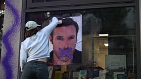 Une militante du collectif NousToutes colle une affiche de Nicolas Bedos sur la façade de la maison d'édition Humensis, le 23 mai 2025 à Paris
