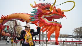 Une femme prend un selfie à côté d'une installation de dragon après une chute de neige à Pékin le 21 février 2024.
