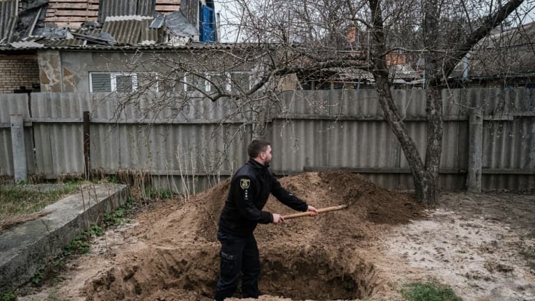 Le policier ukrainien Bogdan Demtsiura exhume le corps d'Andriy Samforskyi, mort à l'âge de 87 ans de maladie le 26 mars 2022 et enterré provisoirement dans son jardin à cause de la guerre, le 19 avril 2022 à Boutcha (Ukraine)