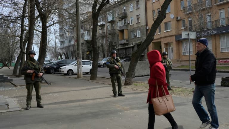 Des piétons passent devant des soldats qui montent la garde devant le bâtiment de l'administration régionale de Mykolaïv touché par des roquettes russes, le 29 mars 2022