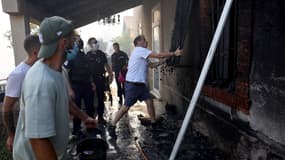Un habitant tente d'enlever un volet de fenêtre pour éteindre un feu de forêt qui se propage dans le quartier de l'Estaque à Marseille, dans le sud de la France, le 8 juillet 2025.