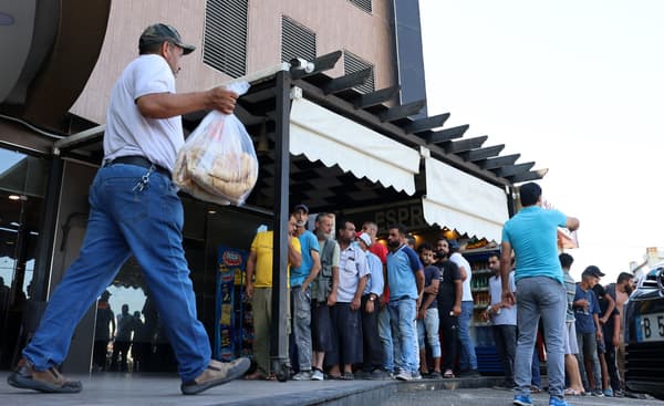 A man walks out of a bakery with a bag of subsidized flatbread, as others continue to queue, in the Lebanese capital Beirut on July 29, 2022, amid a wheat shortage. A man walks out of a bakery with a bag of subsidized flatbread, as others continue to queue, in the Lebanese capital Beirut on July 29, 2022, amid a wheat shortage.