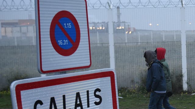 Des migrants, portant des bagages, passent à côté un panneau marquant les limites de la ville de "Calais", le 24 octobre 2016. 