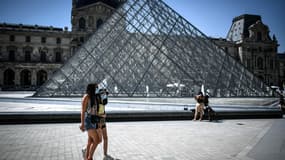 Des touristes masqués devant la Pyramide du Louvre