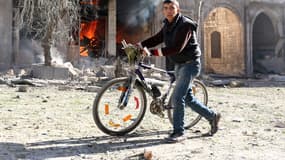 Un jeune homme pousse son vélo près d'une maison en feu, à Alep en Syrie.