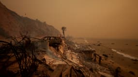 Une voiture brûlée se trouve à côté des restes d'une maison détruite par l'incendie des Palisades, le 8 janvier 2025 à Malibu, en Californie. 