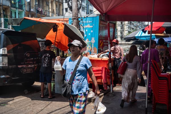 Une femme se promène avec une boisson fraîche sous un parapluie le long d'une rue par une chaude journée à Yangon le 25 avril 2024. 