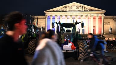 Un piéton passe devant des tracteurs garés devant l'Assemblée nationale à Paris le 13 janvier 2026.