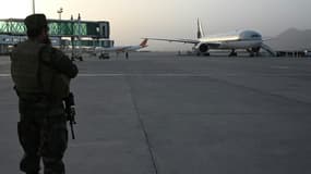 Un combattant taliban monte la garde tandis que des passagers embarquent sur le vol de Qatar Airways à l'aéroport de Kaboul le 10 septembre 2021.