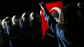 Un manifestant tient un drapeau turc avec une photo du père fondateur de l'État moderne turc, Mustafa Kemal Atatürk, devant des officiers de la police anti-émeute turque lors d'un rassemblement en soutien au maire d'Istanbul arrêté près de l'hôtel de ville d'Istanbul, le 24 mars 2025.