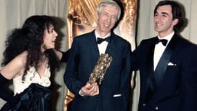 Le cinéaste Michel Deville (C) reçoit le César du meilleur réalisateur pour "Péril en la demeure", le 22 février 1986 à Paris, entouré des comédiens Christophe Malavoy (D) et Carole Laure (G)    