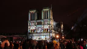 Une foule se tient devant la cathédrale Notre-Dame illuminée lors d'une cérémonie marquant la réouverture de la cathédrale, dans le centre de Paris, le 7 décembre 2024. 