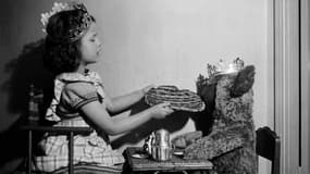 Une petite fille et son ours en peluche mangent une galette des rois pour célébrer l'Épiphanie. Paris, dans les années 50.