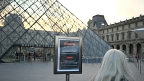 Une femme consulte une affiche informant le public du report de l'ouverture du musée du Louvre, tandis que les employés se réunissent en assemblée générale pour voter sur l'appel des syndicats à une grève illimitée contre la dégradation constante des conditions de travail et la baisse de l'expérience des visiteurs dans ce musée de renommée mondiale, à Paris, le 15 décembre 2025.