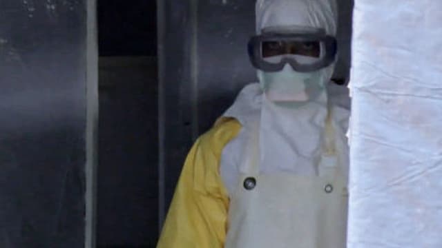 Un homme porte un masque et une combinaison de protection à l'entrée d'une tente médicale à Gueckedou, en Guinée.